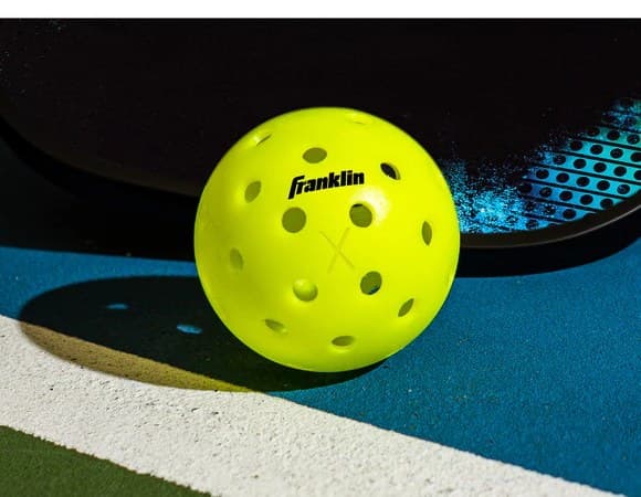 A Franklin X-40 pickleball lit against a dark court beside a paddle