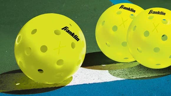 Three Franklin X-40 optic yellow pickleballs resting on a blue and green outdoor court